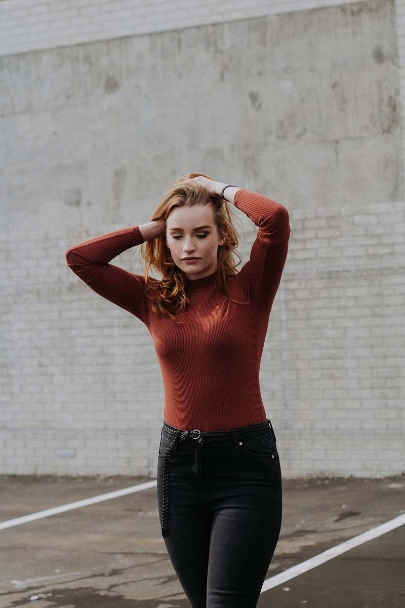 human woman walking while holding her hair near brick wall during daytime people