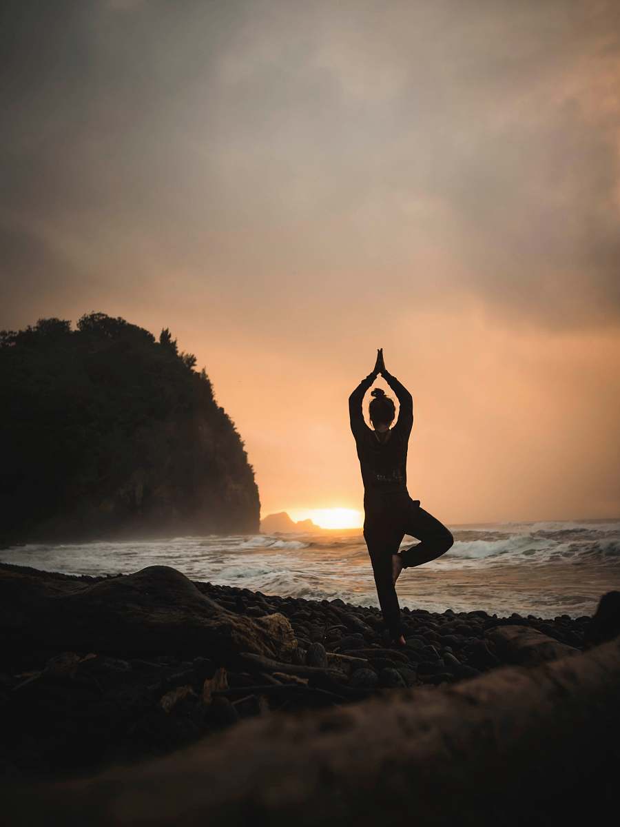 exercise woman doing one-foot yoga stance at the beach under grey sky yoga