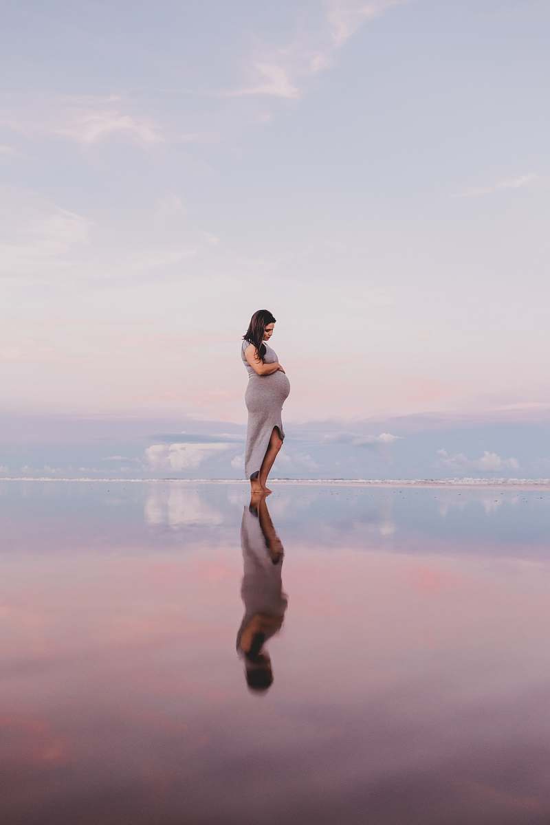 person pregnant woman standing on calm body of water human