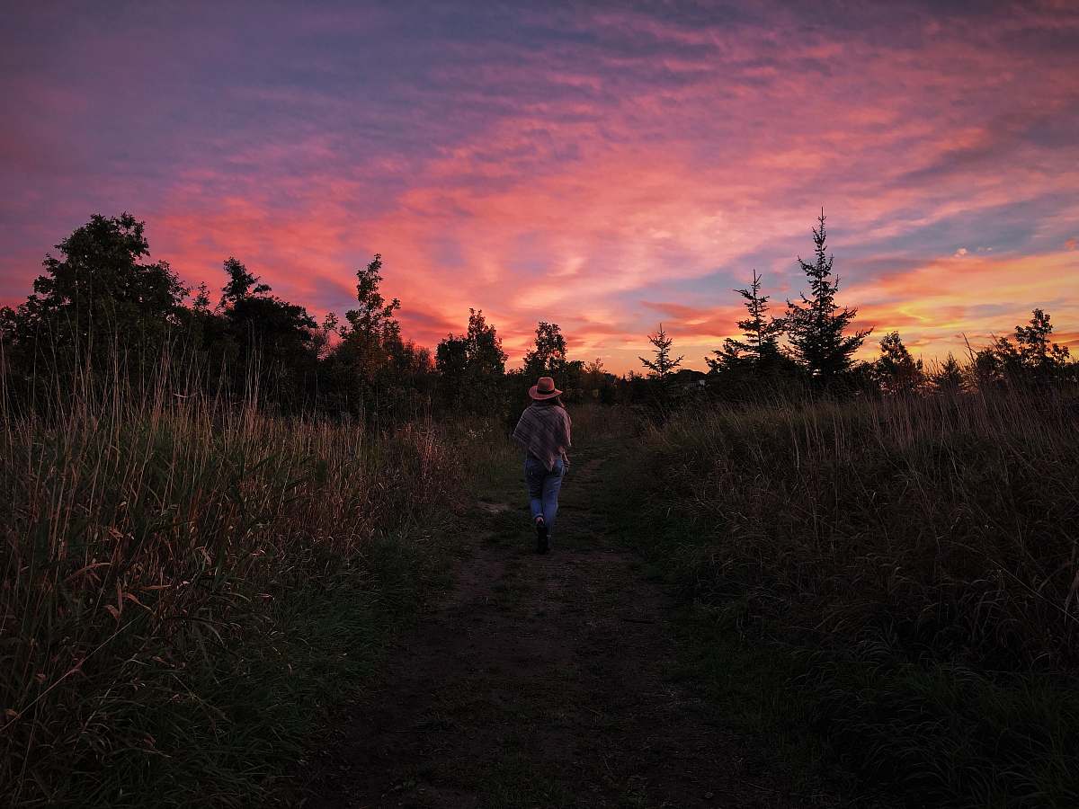 sky woman standing in between grasses dusk