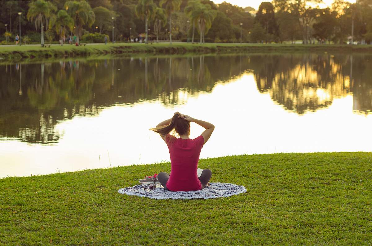 grass woman sitting on mat in front of body of water plant