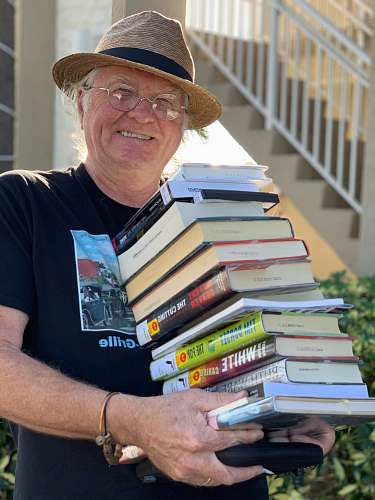 clothing man holding pile of books while smiling human