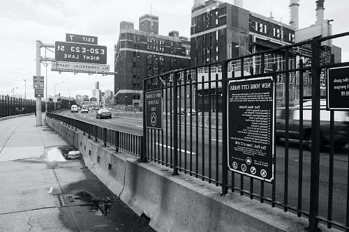 car cars on road beside railing, buildings, and signs black-and-white