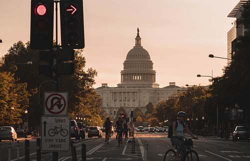 bike people biking on road and different vehicles viewing United States Capitol during daytime screenshot transportation