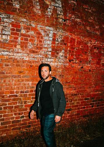 apparel man in black zip-up hoodie walking beside brown bricked wall clothing