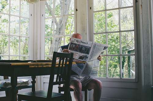 furniture man reading newspaper while sitting on chair window