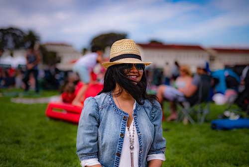 apparel smiling woman while standing on green grass field near peoplle hat