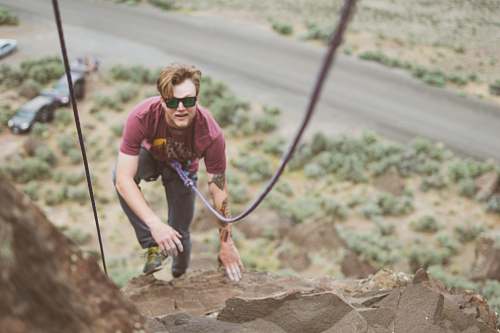 person man in maroon shirt climbing rock formation at daytime people