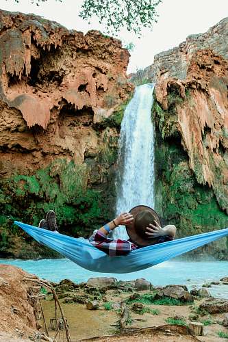 person man laying on blue hammock in front of waterfalls hammock