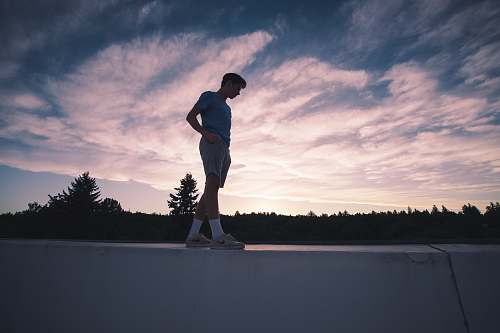 person man standing on white concrete ledge below cloudy sky during dawn people