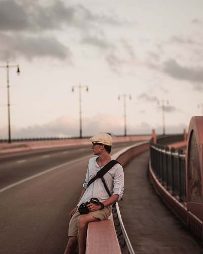 people man wearing grey polo shirt sitting on road railings during daytime person