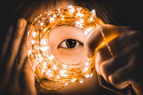 people person covering one eye while holding yellow string lights person