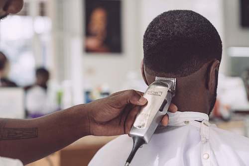 person person holding hair clipper cutting the hair of man sitting people
