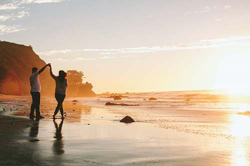 person woman and man holding hands while standing on shore during golden hour el matador state beach