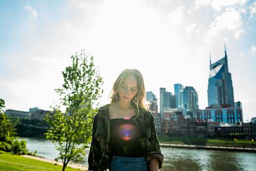 person woman wearing gray and black long-sleeved shirt standing on grass field near river during daytime people