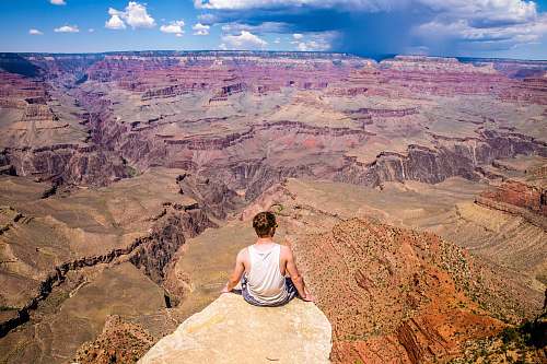 valley person sitting on cliff during daytime canyon