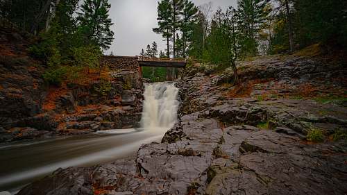 stream bridge above waterfalls during day waterfall
