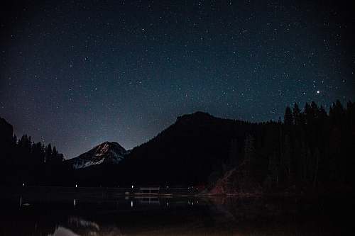 astronomy silhouette of mountain near body of water during night night