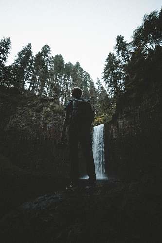 human man standing in front of waterfalls at daytime person