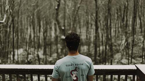person man wearing gray T-shirt standing beside brown wooden railing during snowy day human