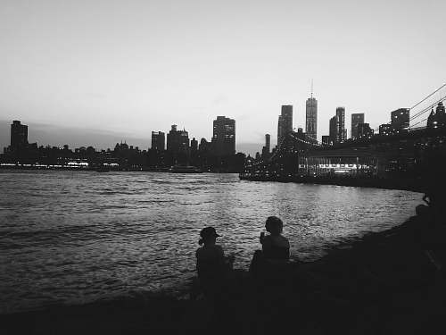human grayscale photo of two women sitting and facing sea black-and-white