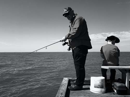 human man in black jacket and pants fishing on sea black-and-white