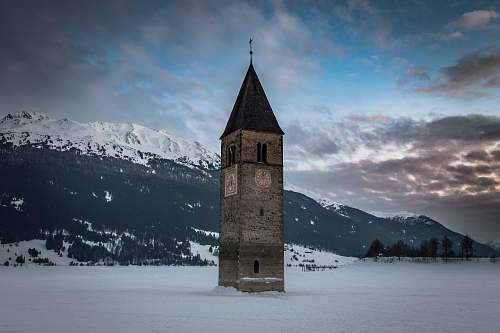 building brown and black clock tower jutting out of white snow covered field tower