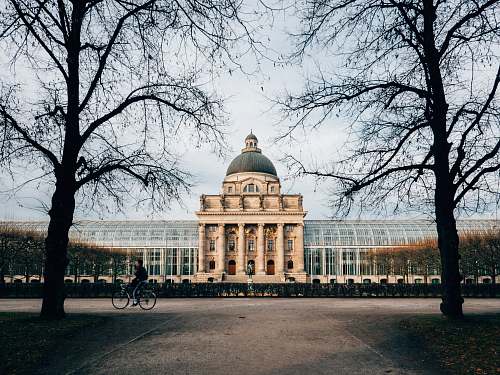 building landscape photo of person riding bicycle in front of castle bayerische staatskanzlei