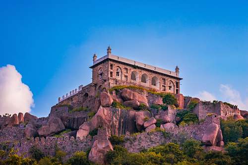 architecture low-angle photography of brown castle on cliff under blue sky housing