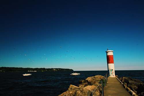 architecture white and red lighthouse near pathway beside rock formation viewing blue sea lighthouse