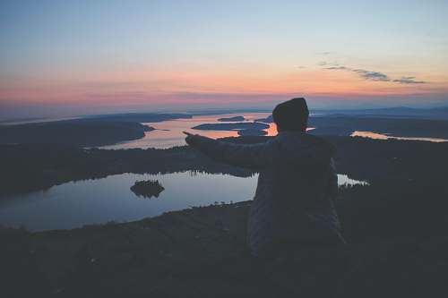 sunrise woman sitting on field near body of water sunset