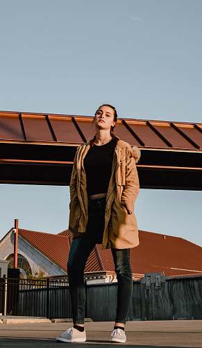 clothing woman in black shirt and brown winter jacket standing on road during daytime footwear