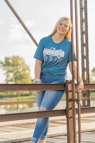 clothing woman in blue crew neck t-shirt and blue denim jeans leaning on brown wooden railings denim