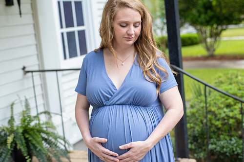 clothing woman in blue v neck dress standing near green plants during daytime human