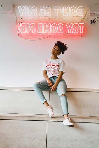 clothing woman in white crew neck t-shirt and blue denim jeans sitting on white concrete wall footwear