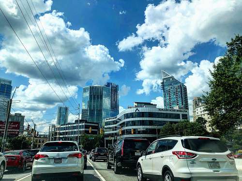 car different vehicles on road viewing city with high-rise buildings under white and blue skies transportation