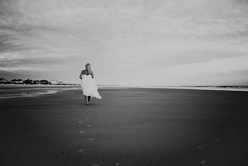 black-and-white grayscale photo of woman walking on seashore grey