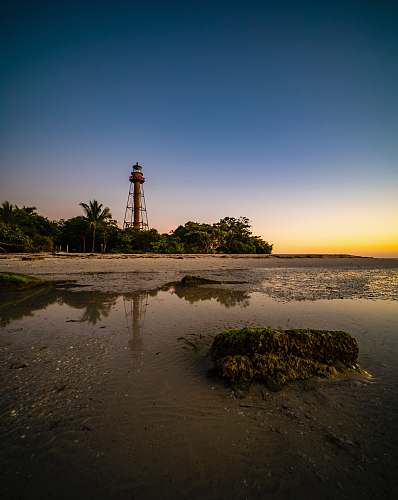 architecture lighthouse on brown sand near body of water during sunset tower