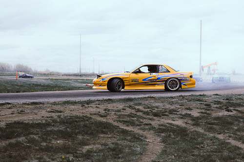 vehicle yellow and blue coupe drifts on black asphalt road during daytime automobile