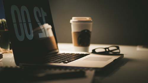 computer grey laptop computer displaying 12:00 on table near coffee cup and eyeglasses pc
