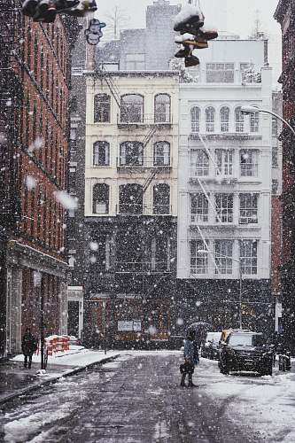 snow person under black umbrella standing on gray asphalt road covered with snow near commercial building and cars during daytime winter