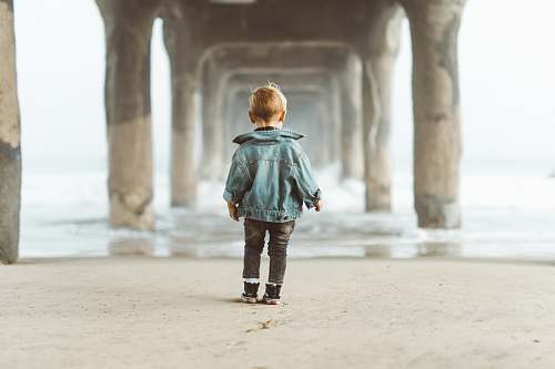 person boy standing on seashore under dock during daytime water