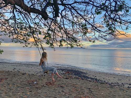 person girl wearing blue romper pants on swing hanging on tree besides seashore 800 olowalu village rd