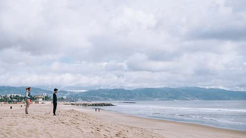 person man and woman standing on sand near ocean during daytime sea