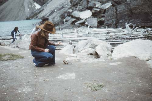 apparel man in brown jacket and blue denim jeans sitting on gray rock during daytime clothing