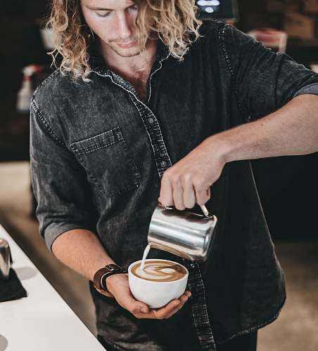 person man wearing black denim jacket pouring white liquid on cup with latte art people