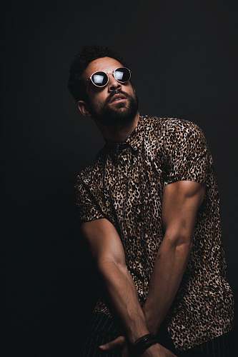 person man wearing brown and black leopard print button-up T-shirt and black sunglasses crossing hands down while looking up people