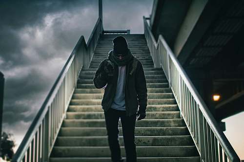 people man wearing brown jacket walking on the stair under black sky person