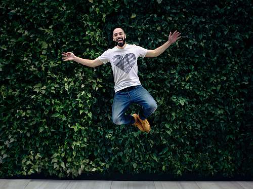 people man wearing t-shirt and jeans jumpshot in front of a green hedge person