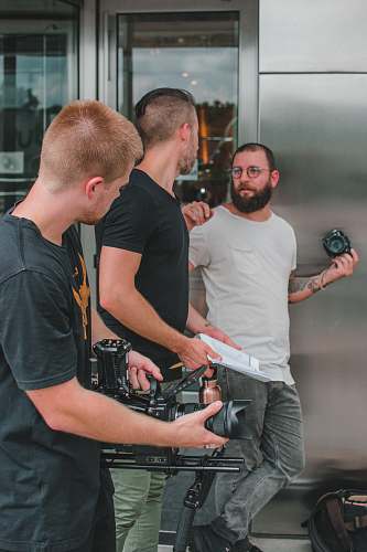 person three men holding cameras beside grey building people
